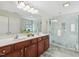 Well-lit bathroom featuring double sinks, wooden cabinetry, and a tiled glass shower with stone flooring at 1127 Woodlands Creek Way, Apex, NC 27502