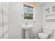 A well-lit bathroom features a pedestal sink, a large mirror, and a toilet underneath a window at 323 Coral Ave, Goldston, NC 27252