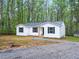 White exterior of house with dark trim and gravel driveway amid a lush, wooded landscape with a shed nearby at 25 Beechnut Ct, Franklinton, NC 27525
