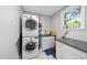 A well-lit laundry room with stacked washer and dryer, granite countertops, sink, and bright window at 108 Ridgepath Way, Cary, NC 27511