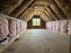 Unfinished attic space featuring insulation, wood framing, and a window, showing potential for customization at 125 Tee Dr, Selma, NC 27576