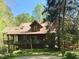 Charming wooden home with a red metal roof, elevated deck, and surrounded by lush trees at 2281 Lamont Norwood, Pittsboro, NC 27312
