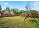 Fenced backyard with green grass, a tree and a swing set with blue skies in the background at 2901 Murray Ridge Trl, Apex, NC 27502