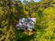An aerial view captures a white house with a metal roof, surrounded by dense trees on a sunny day at 910 Old Orchard Rd, Chapel Hill, NC 27517