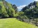 A peaceful backyard featuring a well-kept lawn, mature trees, and a rustic wooden fence under a clear blue sky at 910 Old Orchard Rd, Chapel Hill, NC 27517