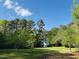 A charming white home surrounded by mature trees and lush greenery against a backdrop of a bright blue sky at 910 Old Orchard Rd, Chapel Hill, NC 27517
