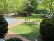 A charming landscape with grass, trees, brick pathway, bird bath, and a lamp post surrounded by lush greenery at 910 Old Orchard Rd, Chapel Hill, NC 27517