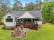 Back of house with deck, outdoor fireplace, white siding, dark trim, lush green lawn and mature trees at 1506 Gormly Cir, Sanford, NC 27330