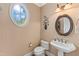 Charming powder room featuring a pedestal sink, toilet, decorative mirror and unique oval window at 2000 Silverleaf Dr, Youngsville, NC 27596