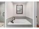 Soaking tub with gray tile surround, modern fixtures, a framed mirror, and adjacent walk-in shower at 305 E First St, Princeton, NC 27569