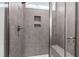 Bathroom shower with glass door featuring gray tile walls, built-in shelving, and a small window at 124 Alta Crest Ln, Garner, NC 27529