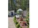 Backyard view with a greenhouse, garden, and shed with a blue door, surrounded by lush greenery and gravel pathway at 255 Williamston Ridge Dr, Youngsville, NC 27596