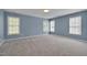 Spacious bedroom with three windows, neutral carpet, and soft blue painted walls at 709 Basil Dr, Durham, NC 27713