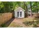 Charming white shed with double doors, nestled among mature trees and a wooden fence at 7433 Deer Track Dr, Raleigh, NC 27613
