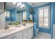 Bright bathroom featuring a double sink vanity, blue walls, and natural light from a window with white shutters at 1809 Green Ford Ln, Apex, NC 27502