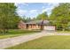 Brick home with a concrete driveway, attached garage, front porch, and lush lawn with scattered trees at 317 William Dr, Benson, NC 27504