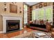 The fireplace stands between two windows with hardwood floors and a leather couch in this traditional living room at 919 Woodham, Pittsboro, NC 27312