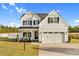 Charming two-story farmhouse exterior with a black roof, white siding, an attached two-car garage, and manicured landscaping at 105 Blooms Way, Kenly, NC 27542