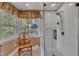 Updated bathroom features a glass enclosed shower, wood chair, and a sunny window overlooking the yard at 1100 Queensbury Cir, Durham, NC 27713
