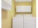 Laundry room with washer, dryer, and overhead storage with bright yellow walls at 117 Vicksburg Dr, Cary, NC 27513
