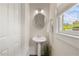 Bright powder room featuring a pedestal sink, round mirror, and window with leafy trees outside at 1093 Trentini Ave, Wake Forest, NC 27587
