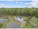 Expansive aerial view of a white farmhouse-style home surrounded by lush greenery and a private pond at 6024 Lunenburg Dr, Raleigh, NC 27603