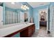 Bathroom with long vanity, wood cabinets, blue walls, ceiling lighting, and an open door to a bedroom at 1027 Upchurch Farm Ln, Cary, NC 27519