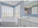 Bright bathroom featuring a soaking tub with glass block window, blue walls, and a vanity with a framed mirror at 175 Bill Avery Rd, Coats, NC 27521