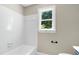 Well-lit bathroom featuring a bathtub, white tile surround, and a window with a view of green trees at 2901 Hunters Bluff Dr, Raleigh, NC 27606