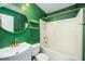 Modern bath with gold fixtures, floating shelves, vanity and shower/tub combo, with striking green walls at 611 Edenberry Dr, Durham, NC 27713