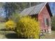 Exterior shot of a rustic shed with red wood walls, yellow flowers, and a metal roof at 7129 Dexter Rd, Oxford, NC 27565