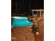 Nighttime view of lighted pool with rock waterfall feature, slide, and lounging area with fireplace at 110 Chapelwood Way, Cary, NC 27518