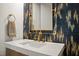 A modern bathroom with a white countertop, gold fixtures, designer mirror and patterned accent wall at 1616 Hunting Ridge Rd, Raleigh, NC 27615