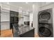 A modern walk-in closet featuring a granite island, custom cabinets, and a stacked washer and dryer at 1616 Hunting Ridge Rd, Raleigh, NC 27615