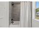 A tiled shower with a black showerhead, white shower curtain, and a window for natural light at 2019 James St, Durham, NC 27707