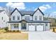 Two-story home with light gray siding, dark trim, three-car garage, covered porch, and a blue front door at 2437 Terri Creek Dr, Fuquay Varina, NC 27526