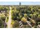 Scenic aerial view of homes surrounded by lush trees, a road, and a distant city skyline at 3100 Coachmans Way, Durham, NC 27705