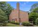 Rear view of the home's brick exterior with a small deck and manicured landscaping at 3100 Coachmans Way, Durham, NC 27705