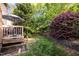 Spacious backyard with a deck, stone retaining wall, and lush green lawn surrounded by trees at 3100 Coachmans Way, Durham, NC 27705