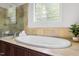 Large soaking tub with travertine surround, next to a glass-enclosed shower and block glass window at 3513 Forest Oaks Dr, Chapel Hill, NC 27514