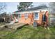 View of the brick home's rear exterior, deck, lawn, and mature tree at 704 N King Charles Rd, Raleigh, NC 27610