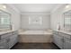 Large soaking tub with tile surround, flanked by granite counters and gray cabinets at 1305 Reservoir View Ln, Wake Forest, NC 27587