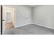 A minimalist bedroom features neutral walls, gray carpet, and a glimpse of a hallway in the open doorway at 203 Sourgum Ct, Zebulon, NC 27597