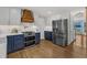 Modern kitchen with stainless steel appliances, blue cabinets, a wooden vent hood, and hardwood floors at 1005 Thorncroft Ln, Apex, NC 27502
