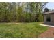 Green backyard with a lush lawn and a border of trees, beside a home with a concrete patio at 1007 Fairhaven Dr, Mebane, NC 27302