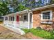 View of exterior featuring a quaint porch, red door, charming brick facade, and lush landscaping at 2506 N Duke St, Durham, NC 27704
