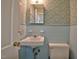 Compact bathroom with a white sink, toilet, light-blue tiled walls, and patterned wallpaper at 4005 King Charles Rd, Durham, NC 27707