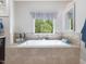 Soaking tub with natural light, light beige tile surround, and decorative window treatment at 6824 Wood Forest Dr, Cary, NC 27519