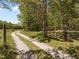 Long gravel driveway leading to a wooded property with mature trees and a rustic gate at 9400 Wheelers Church E Rd, Hurdle Mills, NC 27541