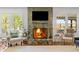 Close-up of a stone fireplace with a lit fire, flanked by comfortable seating and windows at 9400 Wheelers Church E Rd, Hurdle Mills, NC 27541